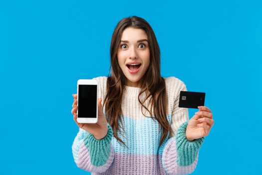 Smiling, excited and fascinated young woman talking about cool new app, banking application, deposit or cashback service, holding smartphone facing display camera, credit card, grinning amused.