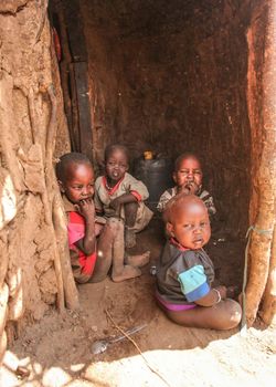 Unknown Masai village near Amboselli park, Kenya - April 02, 2015: Group of poor dirty children with faces and mouth covered with flies sitting at entrance to their hut.