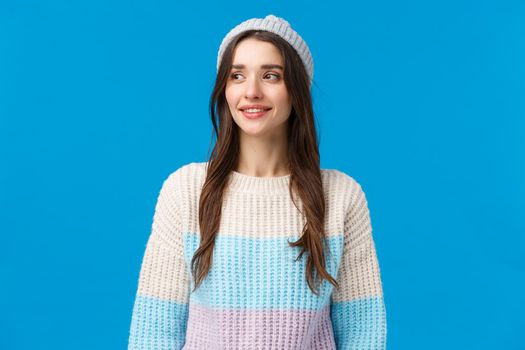 Waist-up portrait curious happy cute girl in winter hat, sweater looking around waiting for friend play snowballs, enjoying holidays, smiling broadly, standing blue background enthusiastic.