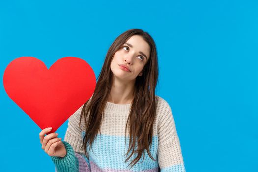 Love is for dorks. Unimpressed and unbothered, careless attractive college girl, eye roll and looking away uninterested, holding big red heart, dong care on valentines day, standing blue background.