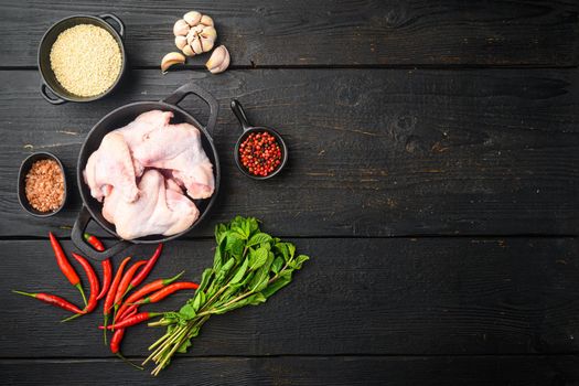 Uncooked chicken wings with spices set, and sesame, in frying cast iron pan, on black wooden table, top view flat lay, with copy space for text