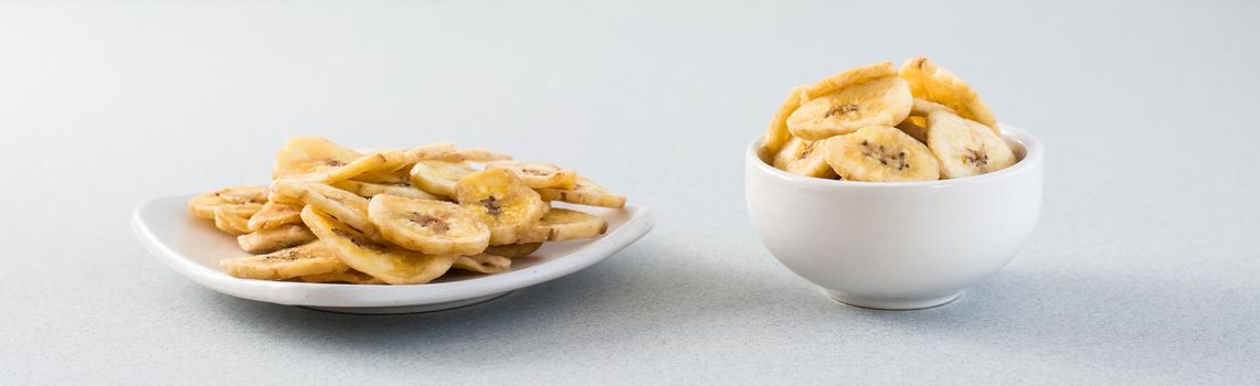 Baked banana chips in a white bowl and saucer on the table. Fast food. Web banner