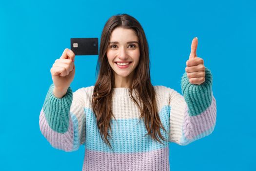 Waist-up portrait satisfied young woman smiling recommend bank, received her scholarship, show thumb-up, credit card, nod approval and agreement, like new features, cashback, blue background.