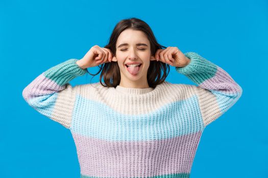 Waist-up portrait funny and cheerful, playful attractive woman in winter sweater, wishing happy holidays, enjoying christmas season, leisure time, showing tongue, grimacing, pulling ears.