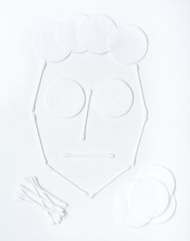 Female face made of cotton pads and cotton swabs on a white background. Facial skin care concept. Top view