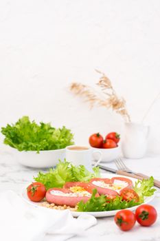 Romantic breakfast. Fried eggs in heart shaped sausages, lettuce and cherry tomatoes on a plate on the table. Vertical view. Copy space