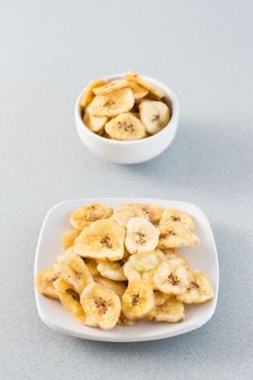 Baked banana chips in a white bowl and saucer on the table. Fast food. Web banner. Vertical view