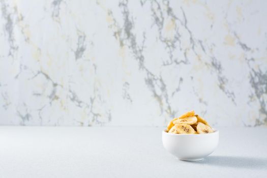 Banana chips in a white bowl on the table. Fast food. Copy space