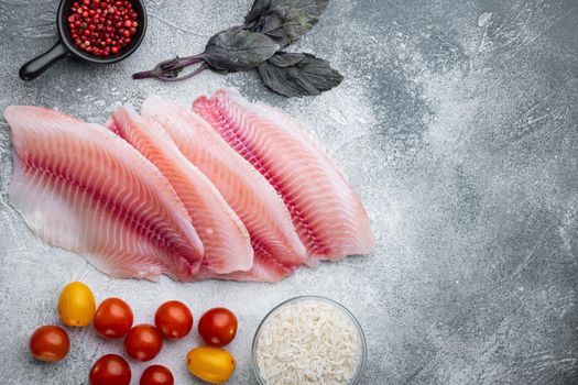 Raw white fish tilapia, with basmati rice and cherry tomatoes ingredients, on gray background, top view with copy space for text