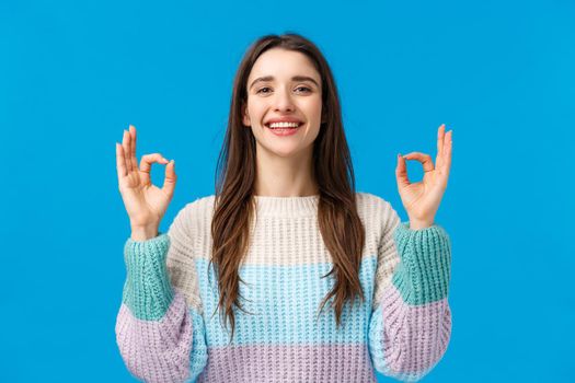 Happy charismatic gorgeous woman in winter sweater, say yes, alright, showing okay gestures, rate excellent movie, perfect gift, spend awesome holidays on winter ski resort, blue background.