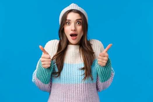Surprised and happy amazed young brunette woman in winter hat, sweater, stare camera impressed, gasping hold breath speechless staring awesome thing and show thumbs-up in like, yes gesture.