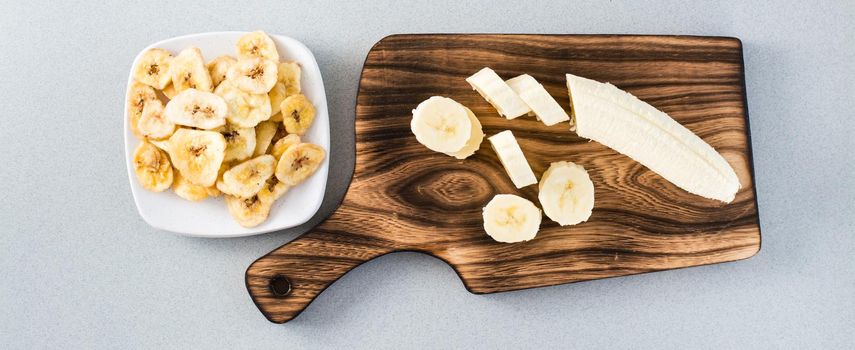 Banana slices on a cutting board and banana chips on a saucer on the table. Fast food. Web banner