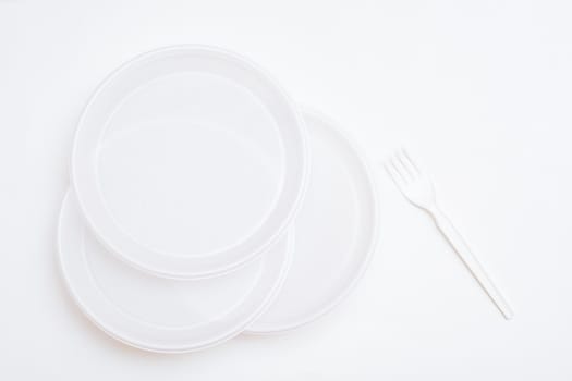 Three white disposable clean plastic plates and a fork on a white background. Top view