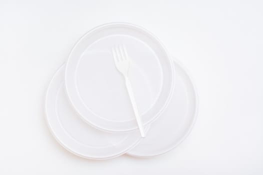 Three white disposable clean plastic plates and a fork on them on a white background. Top view