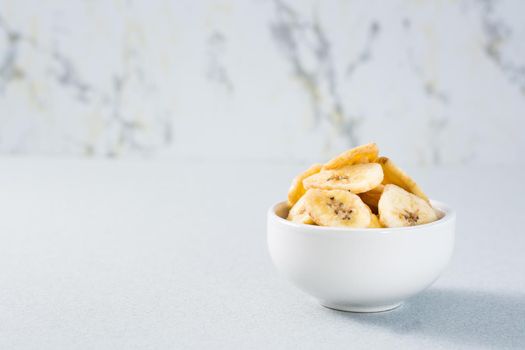 Banana chips in a bowl on the table. Fast food. Copy space