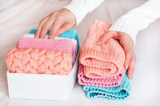 Organization and order. Female hands fold knitted clothes in a pile next to a box with neatly folded things