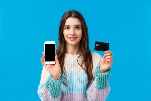Waist-up portrait assertive young woman smiling, showing how banking system works, connect bank account with smartphone application, holding credit card and mobile, showing something on display.