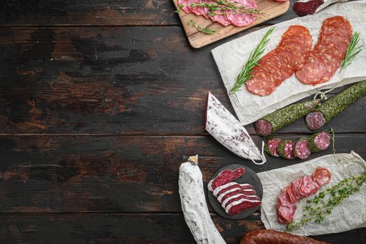 Variety of dry cured chorizo, fuet and other sausages cut in slices with herbs on old wooden table, top view with copy space.