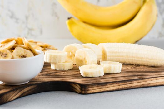 Banana slices on a cutting board and banana chips in a bowl on the table. Fast food.