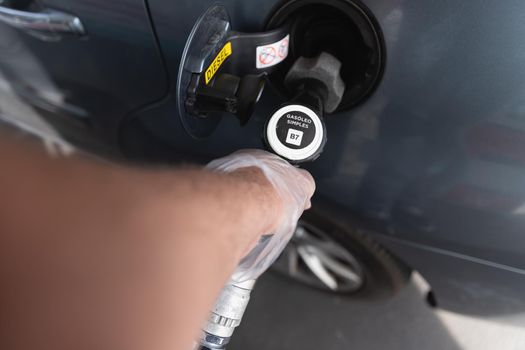 man filling the fuel tank of his car while wearing a plastic glove. On the diesel gun, it is written in Portuguese simple gasoleo (simple gasoil)