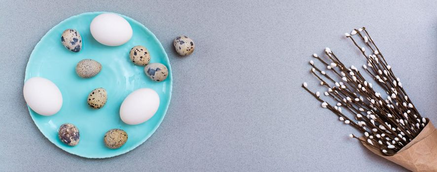 Happy Easter. Chicken and quail eggs on a plate and packaging with pussy willow branches on a gray background. Top view. Web banner