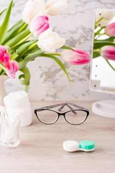 Low vision and the choice between glasses and lenses. Container for lenses in front of glasses, hygiene products and mirrors on the table. vertical view