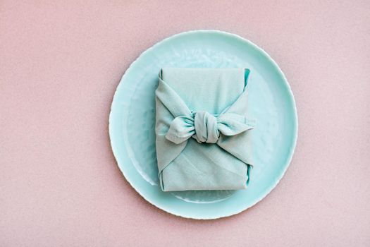 Eco-friendly gift - a box wrapped in cloth on a plate on a gray background. Minimalism