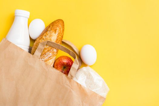 Food delivery concept. Bread, milk, eggs, cereals and fruits in a paper bag on a yellow background
