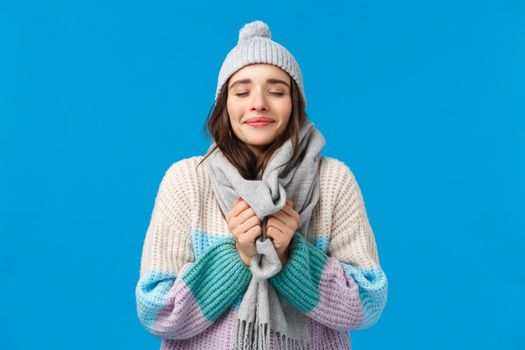 Happiness, dreams and christmas mood concept. Cheerful attractive sensual young woman in winter hat, sweater, touching scarf around neck, close eyes and inhale fresh air, enjoy snowy weather.