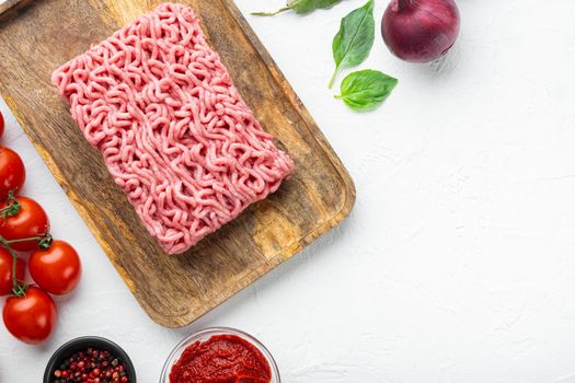 Ingredients for cooking Bolognese sauce, minced beef meat tomatoe and herbs set, on wooden tray, on white stone background, top view, flat lay, with copy space for text
