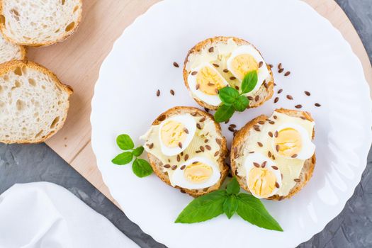 Hearty breakfast in the morning. Fresh baguette sandwiches with butter, quail eggs, flax seeds and basil seeds on a plate on the table. Top view. Close-up