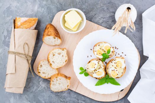 Hearty breakfast in the morning. Fresh baguette sandwiches with butter, quail eggs, flax seeds and basil seeds on a plate on the table. Top view