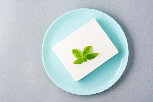 A piece of fresh feta cheese and basil leaves on a plate on the table. Ingredient for Greek salad. Top view
