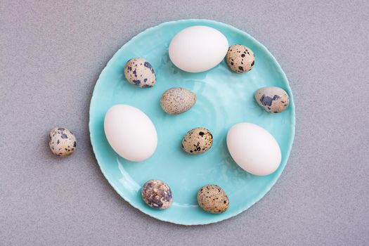 Happy Easter. Chicken and quail eggs on a plate on a gray background. Top view