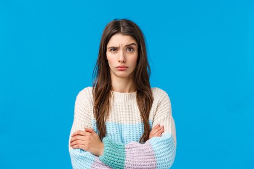 Skeptical, annoyed and displeased young woman hearing something stupid, nonsense, raise eyebrow suspicious and doubtful, cross hands over chest with disapproval, standing blue background.