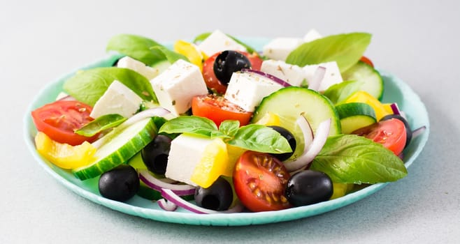 Fresh homemade greek salad with basil leaves on a plate on the table. Domestic life. Web banner