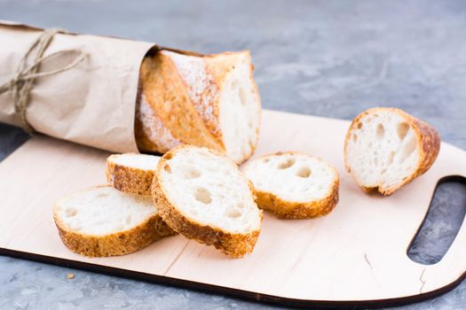 Fresh baguette in wrapping paper cut into pieces on a cutting board on a table