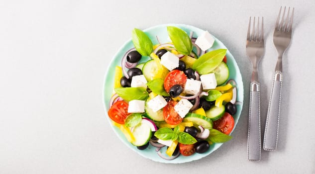 Fresh homemade greek salad with basil leaves on a plate and forks on the table. Domestic life. Top view. Copy space. Web banner