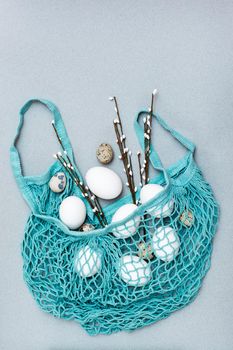 Happy Easter. Eggs and pussy willow branches in a mesh bag on a gray background. Top view