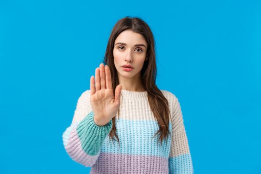 Please stop. Serious-looking assertive and confident young attractive woman pulling hand forward in prohibition, disapproval motion, show restriction telling enough, no sign, standing blue background.