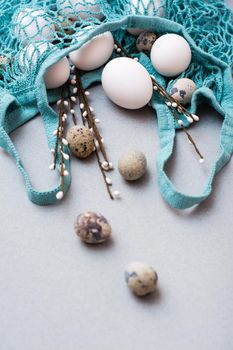 Happy Easter. Eggs and pussy willow branches in a string bag on a gray background. Vertical view