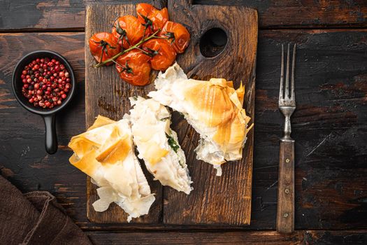 Freshly cooked Chicken Kiev oozing garlic and parsley butter set, with baked cherry tomatoes, on serving board, on old dark wooden table background, top view flat lay