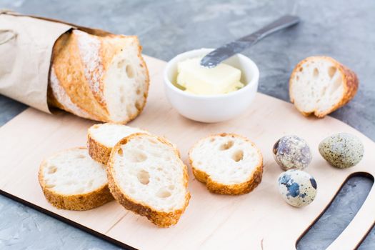 Cooking a hearty breakfast with fresh baguette, butter and quail eggs on a cutting board on a table