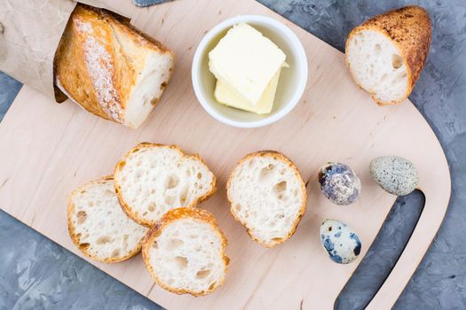 Cooking a hearty breakfast with fresh baguette, butter and quail eggs on a cutting board on a table. Top view. Close-up