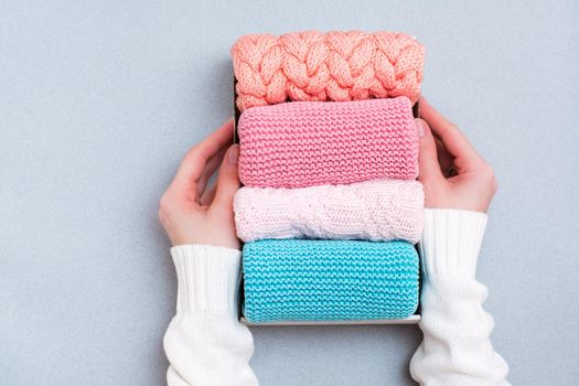 Organization and order. Women's hands hold a box of neatly folded knitted clothes. Top view