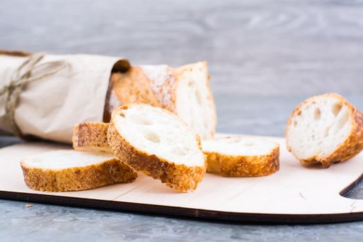 Fresh baguette in wrapping paper cut into pieces on a cutting board on a table. Close-up