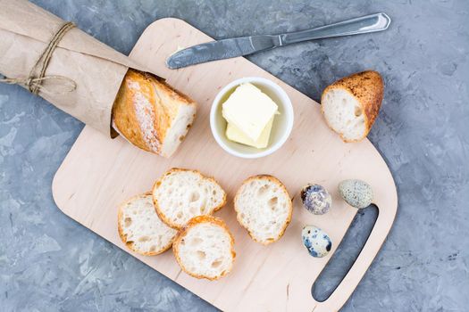 Cooking a hearty breakfast with fresh baguette, butter and quail eggs on a cutting board on a table. Top view