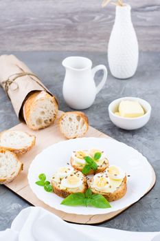 Hearty breakfast in the morning. Fresh baguette sandwiches with butter, quail eggs, flax seeds and basil seeds on a plate on the table. Vertical view