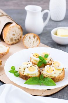 Hearty breakfast in the morning. Fresh baguette sandwiches with butter, quail eggs, flax seeds and basil seeds on a plate on the table. Vertical view. Close-up