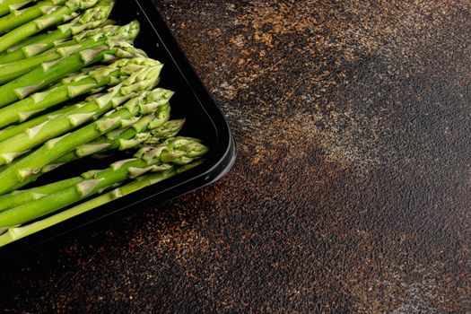Bunch of fresh asparagus set, in plastic market container, on old dark rustic background, with copy space for text